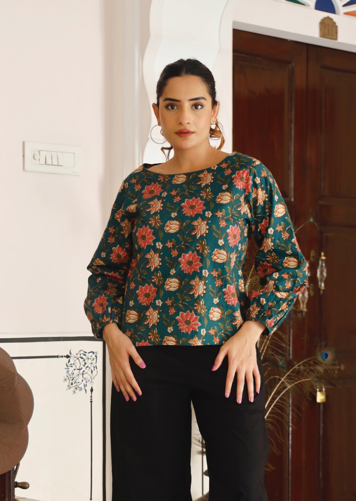Woman wearing loose fit cotton top in pink, cream and orange floral print on deep green base.