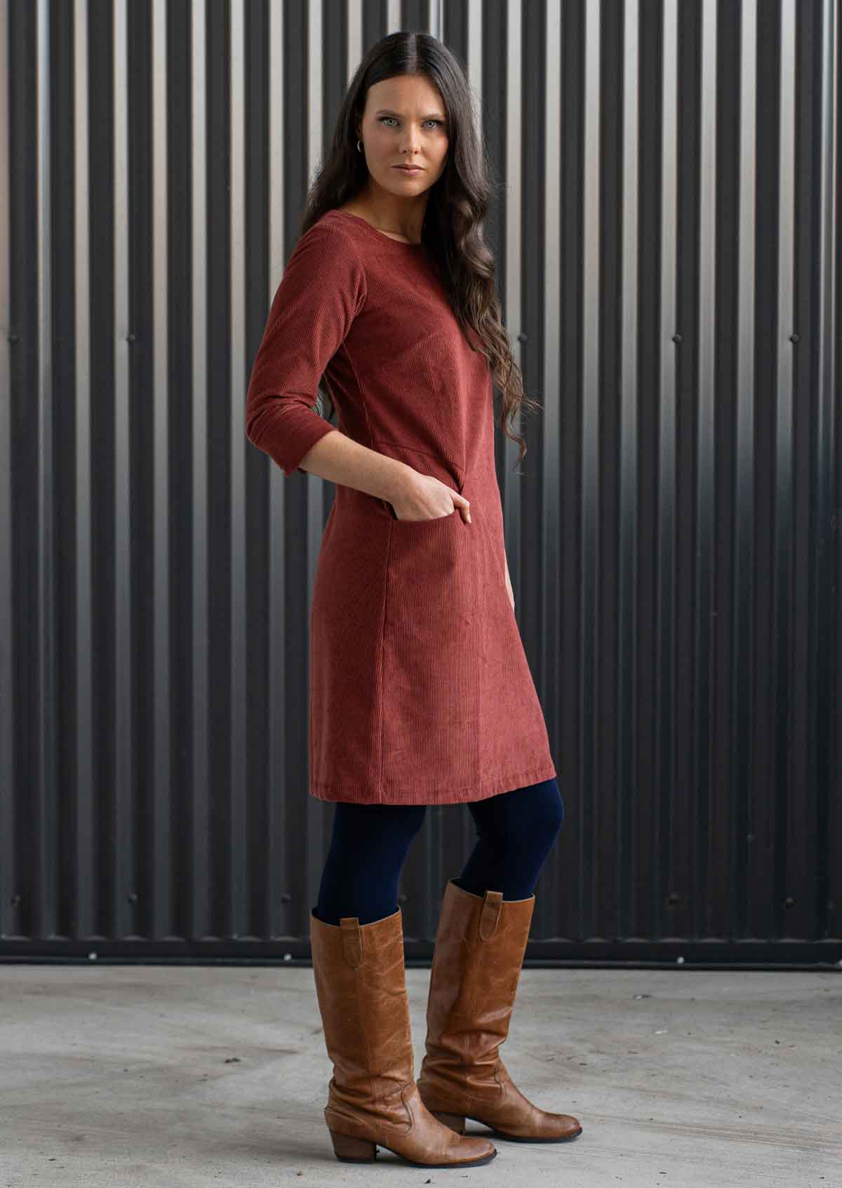 Woman wearing rust coloured corduroy tunic with sleeves over navy blue leggings and boots