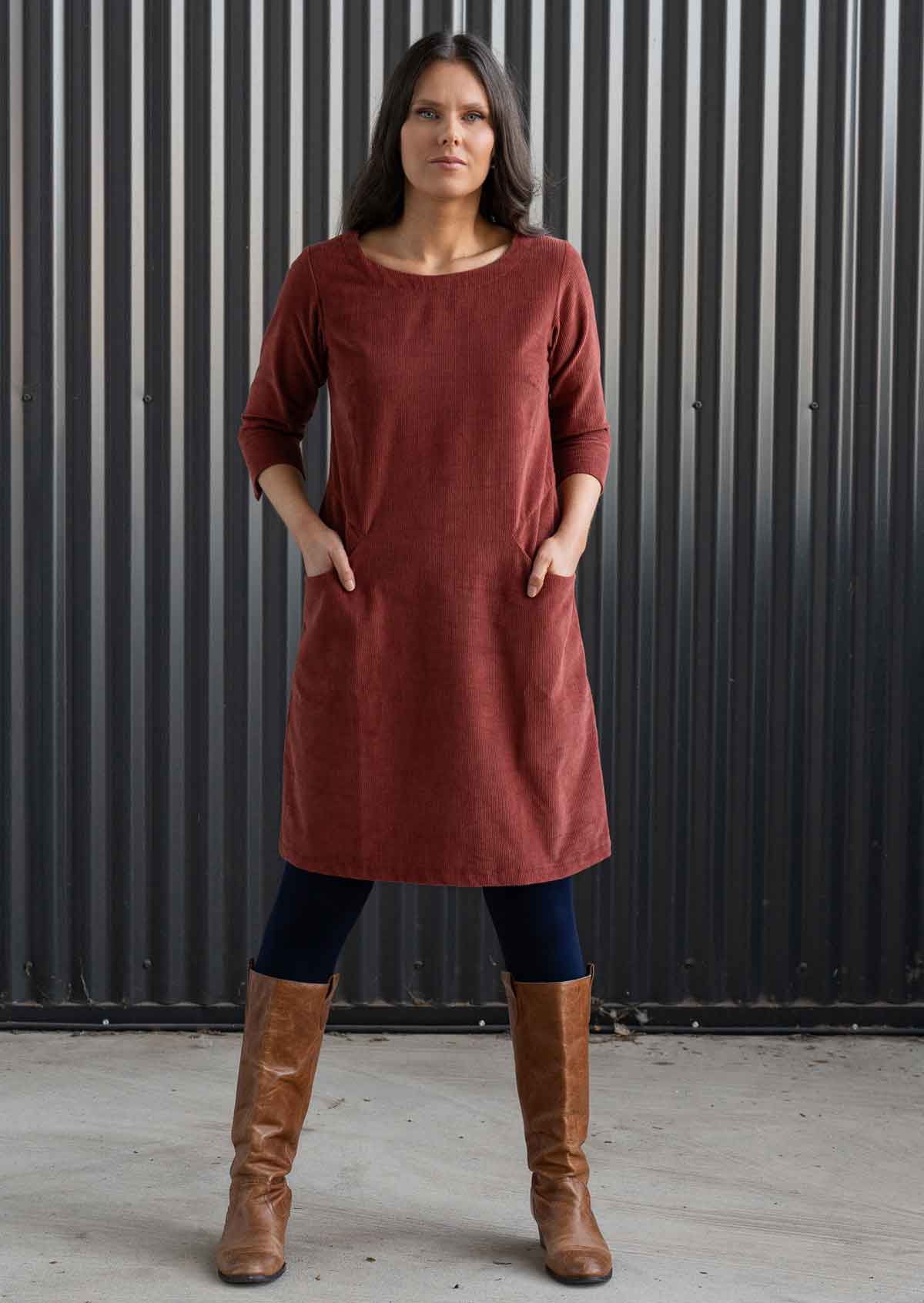 Woman wearing rust coloured cotton corduroy dress with sleeves over navy blue leggings and boots