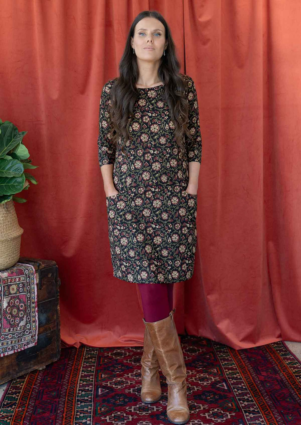 Model posing in knee length cotton dress with round neckline, 3/4 sleeves and hands in pockets.