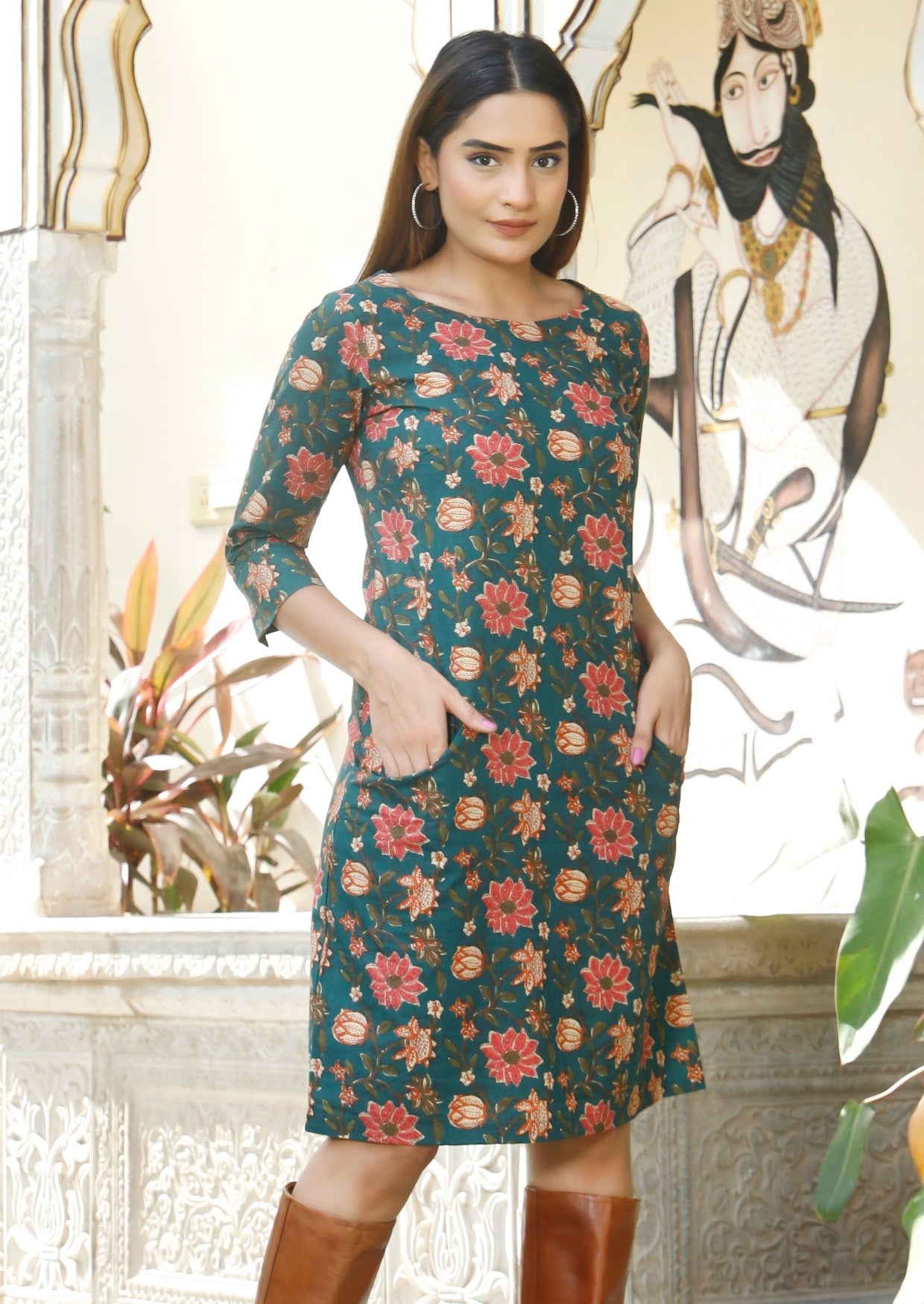 Model standing with hands in pockets wearing a knee length, floral printed cotton dress with 3/4 sleeves and pockets.