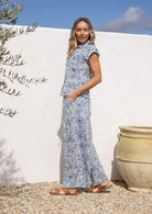 Woman in a white based blue floral cotton pant against a white wall.