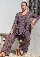 Woman seated on a edge of wooden stool pairing dark purple wide leg cotton pants with long sleeve cotton top.