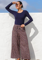 Woman wears wide leg cotton pants in deep purple with pink, cream floral print.