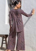 Women standing in back facing pose wearing a dark purple based floral printed cotton pants with a cotton top in same print.