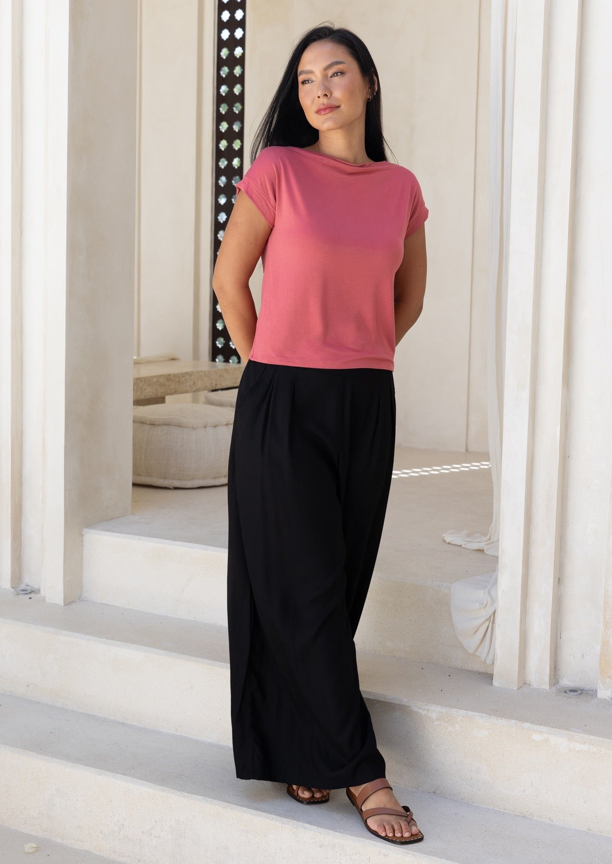 Woman wearing a pink top and black wide leg rayon pants standing on steps