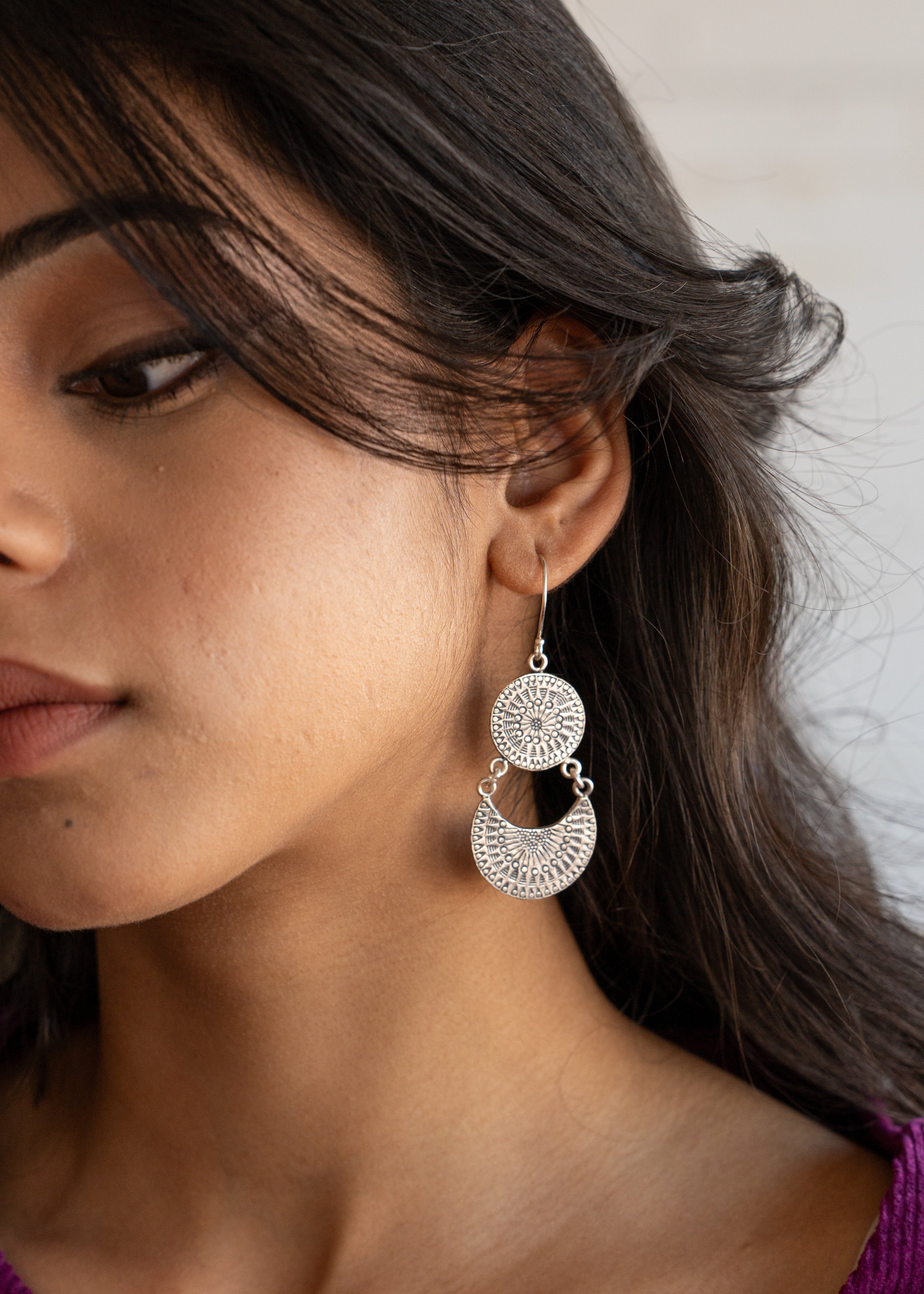 Close-up of a woman wearing silver earrings with a neutral background