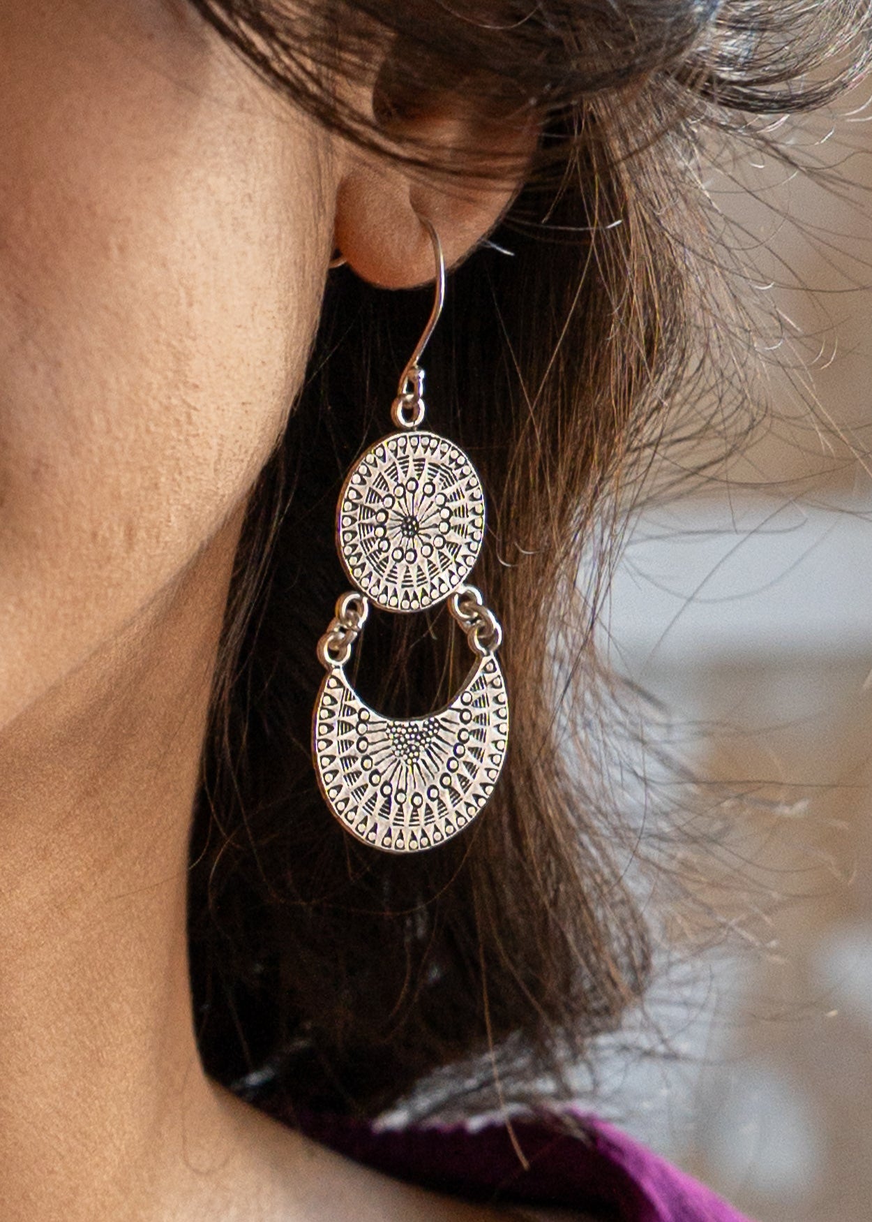 Close-up of a person wearing large silver hill tribe earrings with a blurred background