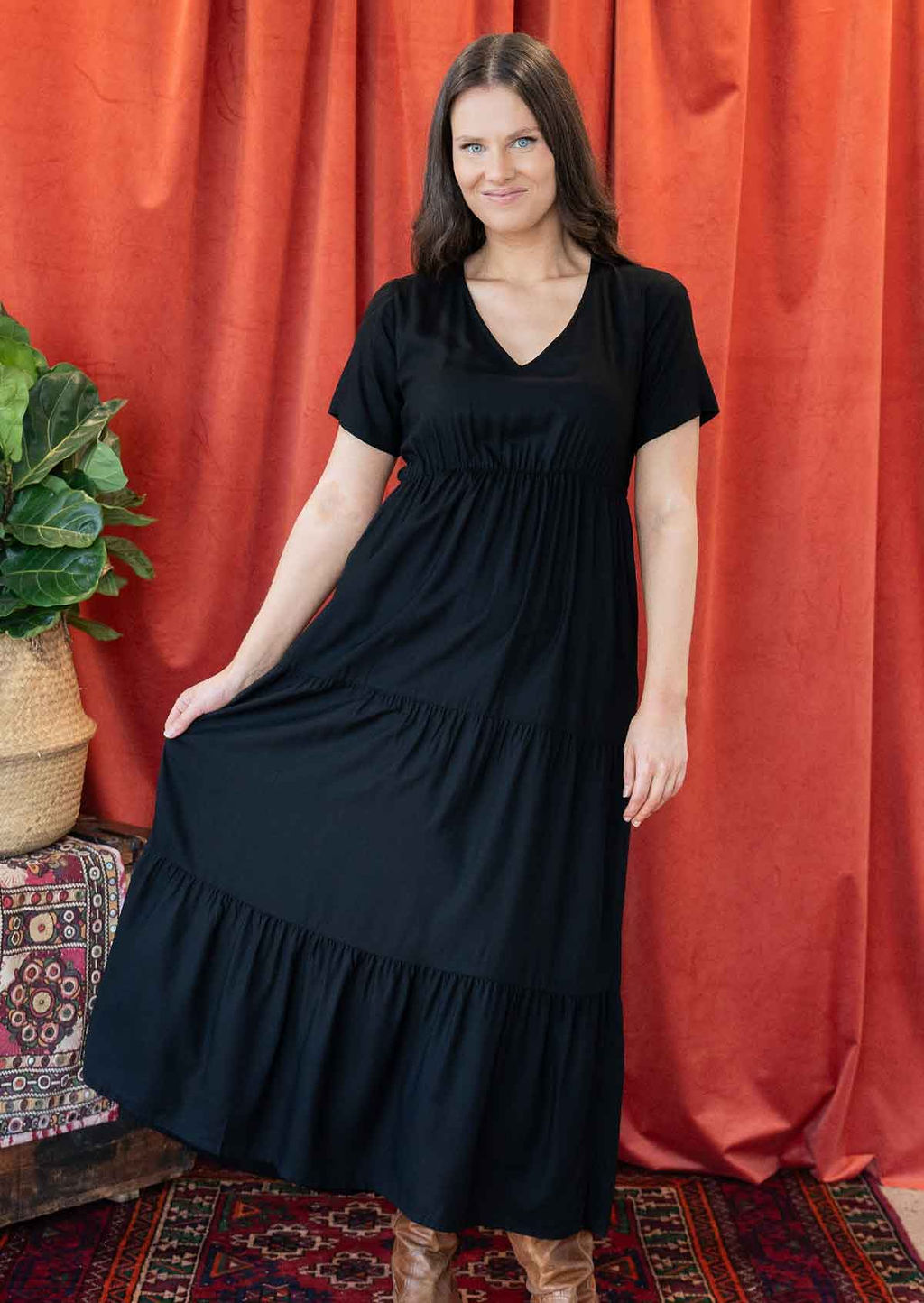 Woman wearing a black rayon maxi dress, holding the side out to display the tiered skirt