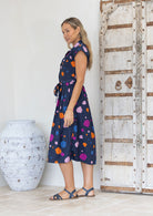 Woman stands side on in a navy based cotton midi length dress with colourful spots
