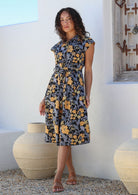 Model posing in a black retro floral print shirt style 100% cotton dress with cap sleeves and detachable waist tie