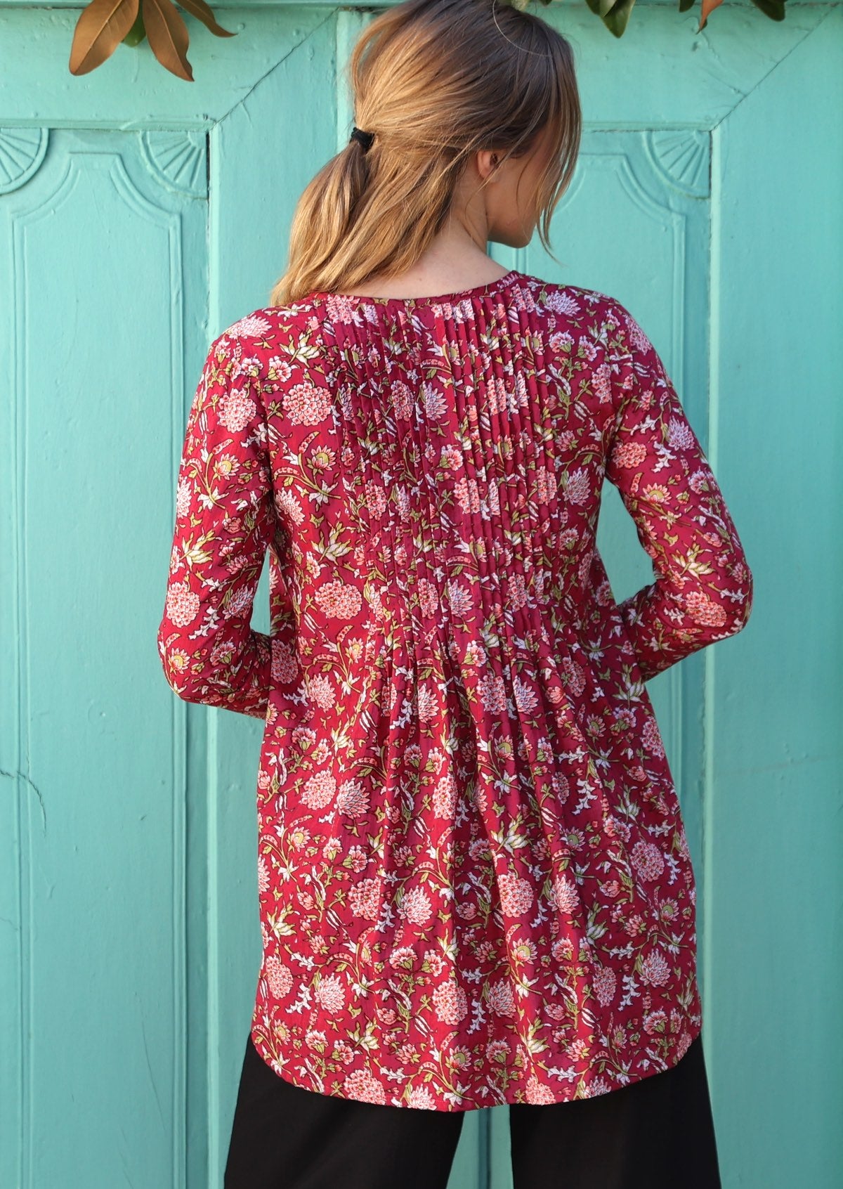 Woman wears cotton long sleeve top with small pin tucks across front and back of bodice, in floral print with cranberry base