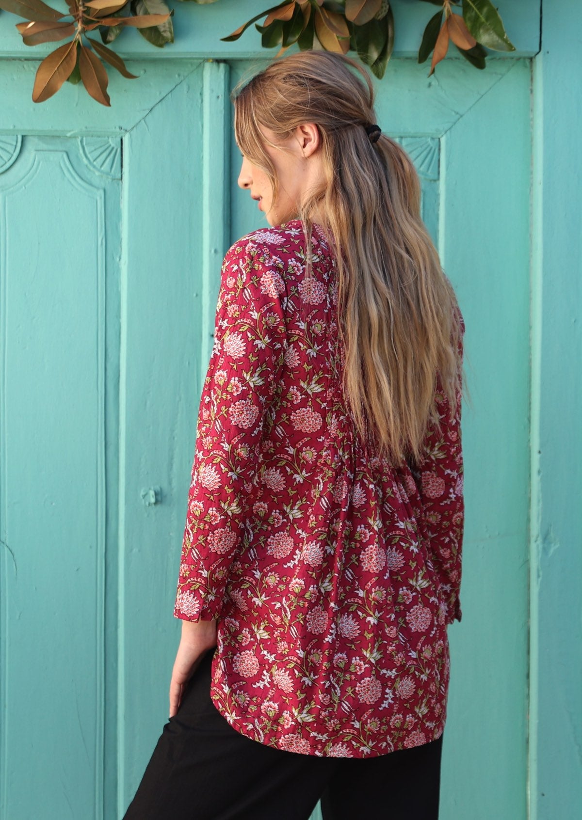 Woman wears cotton long sleeve top in floral print with cranberry base, that is longer at the back
