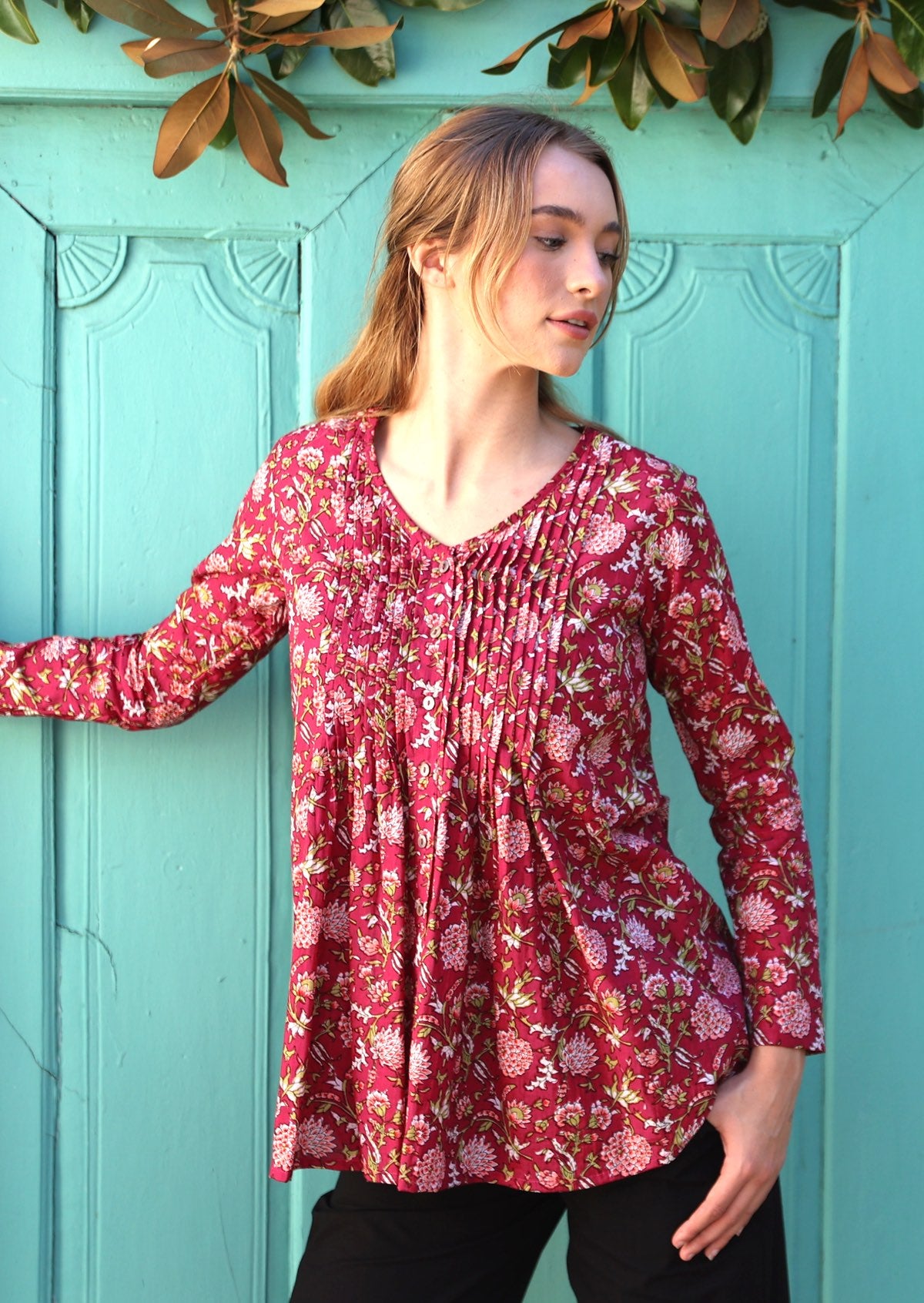 Model poses in long sleeve button through top with V-neckline and small pin-tucks across chest that leads into flared base