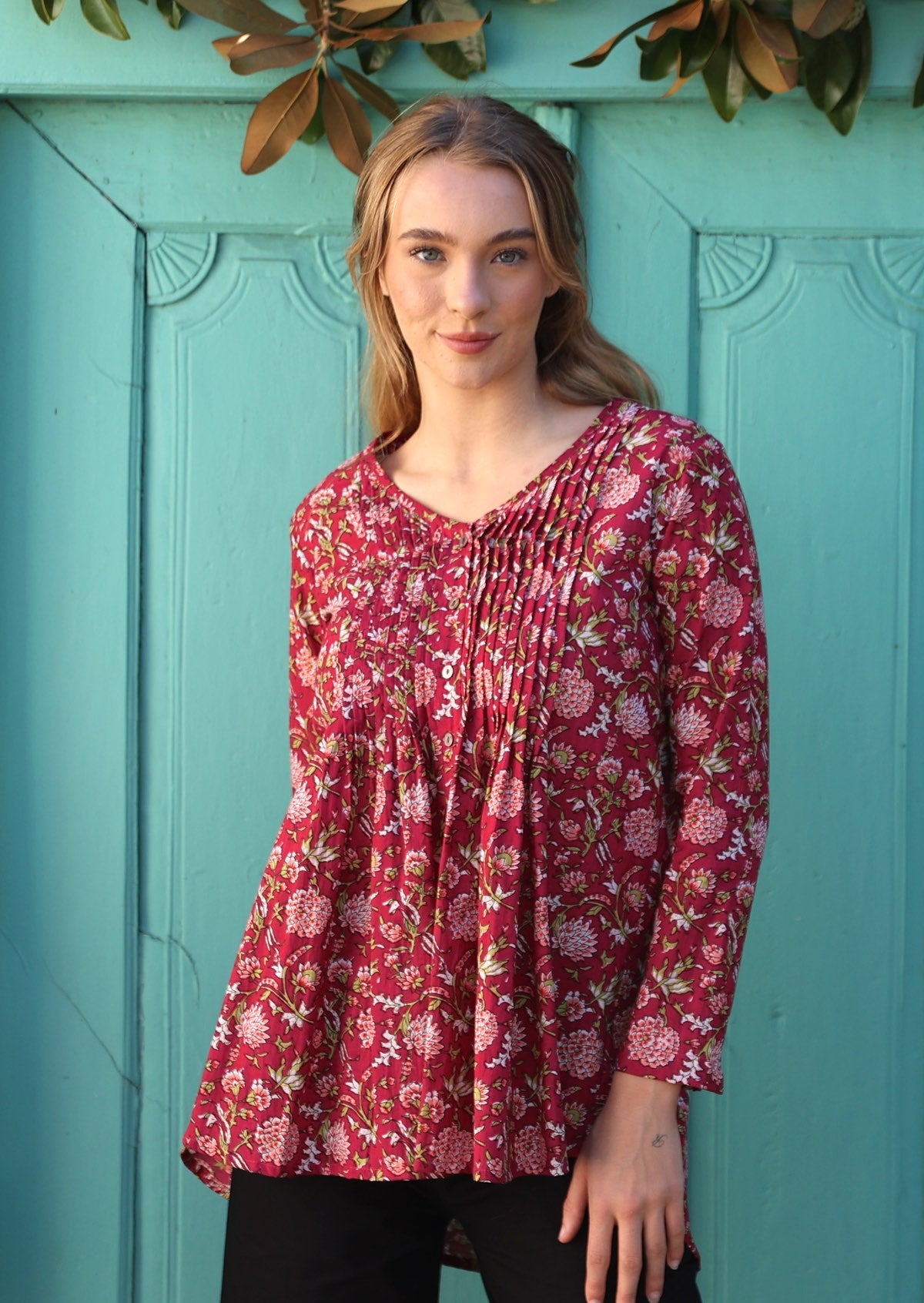 Woman poses in cotton long sleeve button through top with small pin tucks across chest in floral print with cranberry base