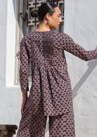 Woman wears cotton long sleeve top with longer back and small pin tucks across front and back of bodice.