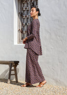 Side pose of model wearing cotton long sleeve, button through top in dark purple with wide leg, floral printed pants.