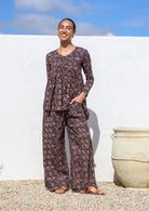 Model poses in long sleeve button through top with V-neckline and small pin-tucks across chest that leads into flared base