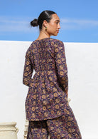 Woman wears cotton long sleeve top with small pin tucks across front and back of bodice, that is longer at the back.