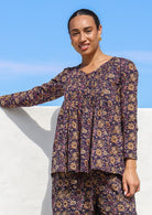 Woman in cotton long sleeve button through top with small pin tucks across chest in dark purple based floral print.