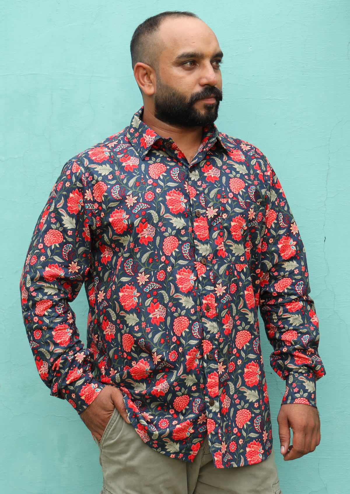 Man wearing a red floral print on a blue base cotton long sleeve shirt against an aqua background