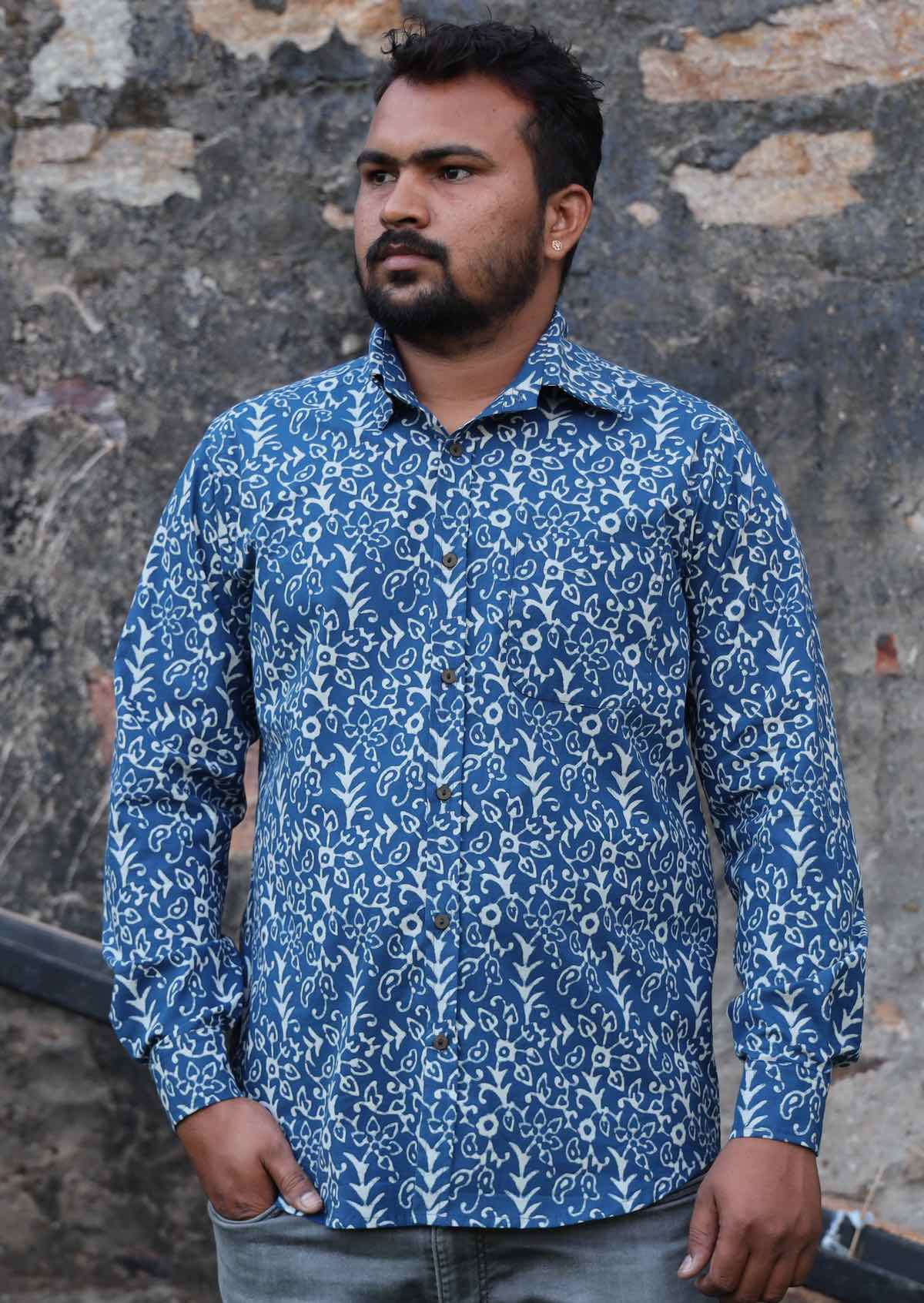 Man stands in button through cotton long sleeve shirt in a white Indian floral print with a blue base