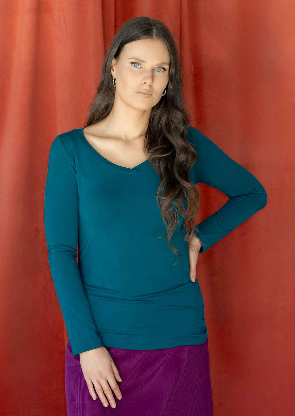 Woman wearing a teal long sleeve stretch v-neck soft rayon top over purple corduroy skirt