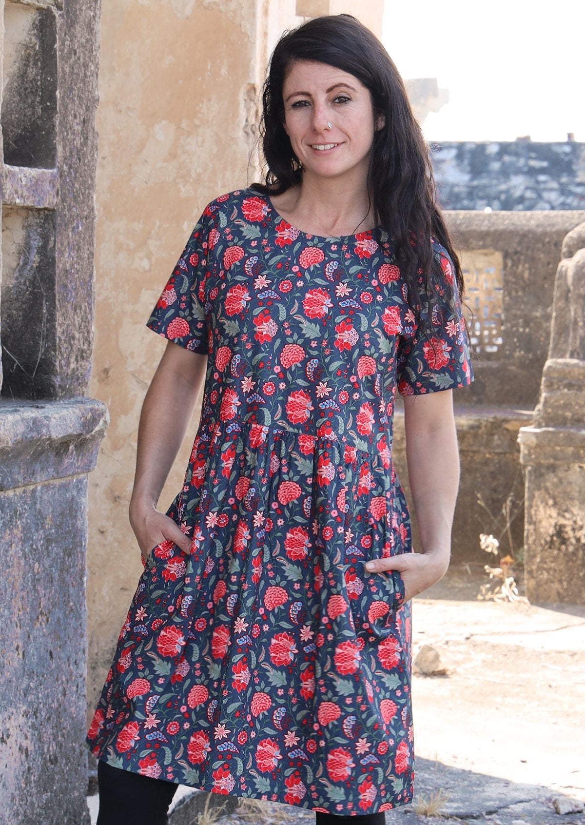 Woman wearing 100 percent cotton blue base retro dress with leafy and floral print with both hands in pockets