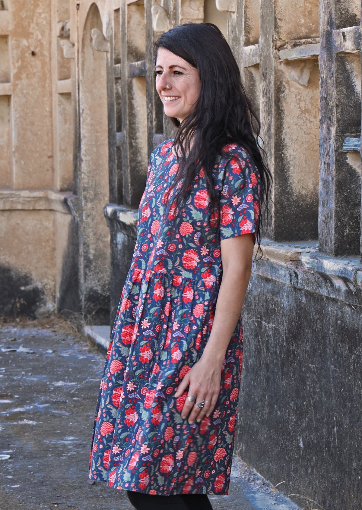 Woman smiling and standing sideways wearing 100 percent cotton blue base retro dress with leaf and floral print