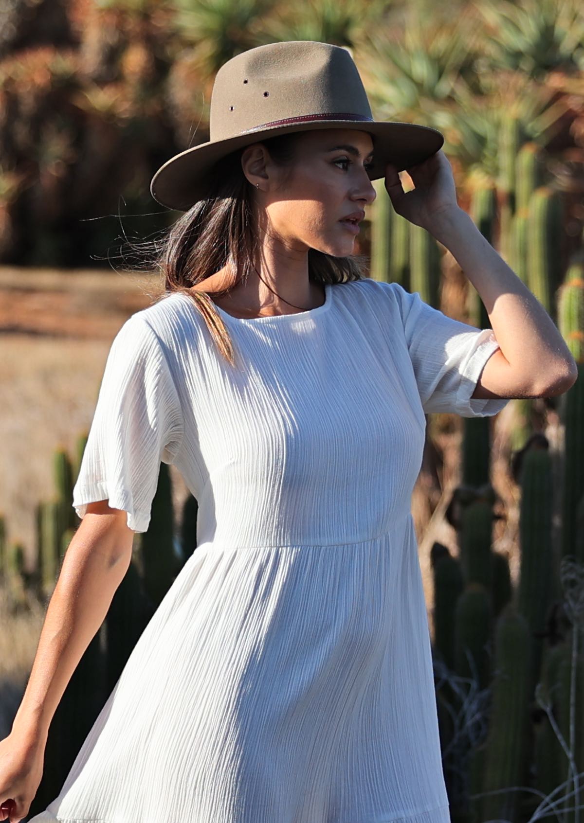 woman wearing white 100% cotton maxi dress with hat in front of cacti