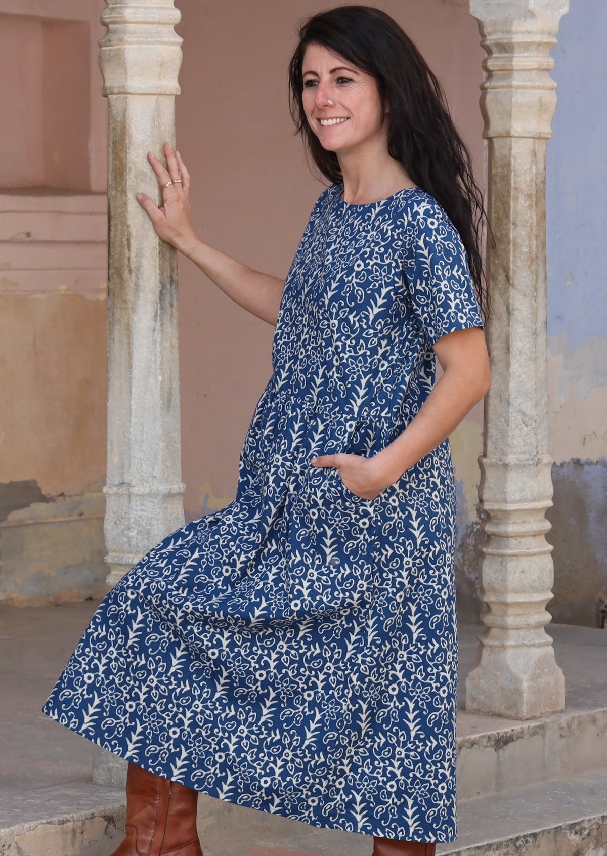 Woman leaning on pillar with one hand and the other hand in a pocket wearing 100% cotton blue and off white Maddison dress