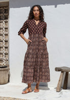 Woman wearing a brown Indian Cotton maxi dress standing against a white wall with hands in pockets