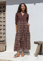 Woman wearing a brown floral Indian Cotton maxi dress standing against a white wall with hands in pockets