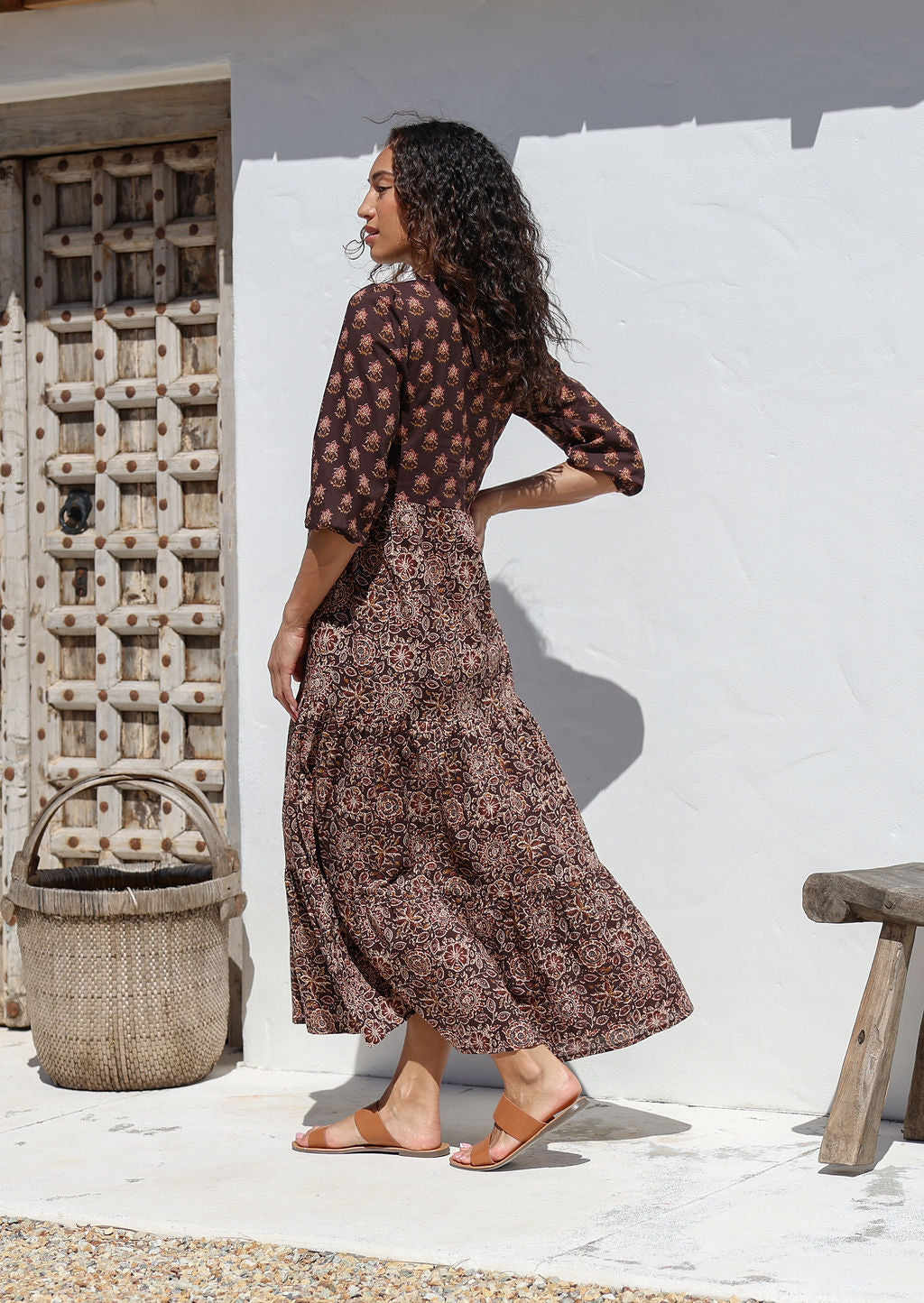 Woman in a floral cotton dress standing against a white wall with rustic elements.