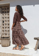 Woman in a floral cotton dress standing against a white wall with rustic elements.