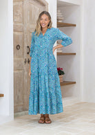 Model with her hand on hip wears 100% cotton white and blue floral print maxi dress with buttoned bodice.