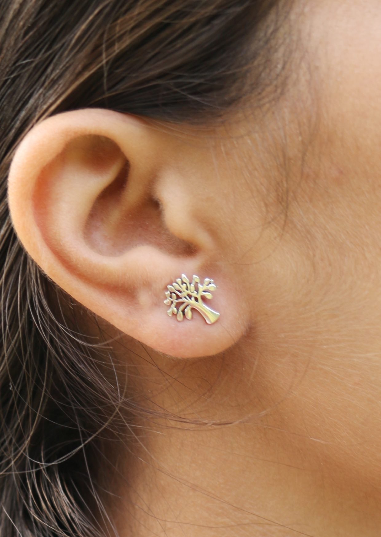 Person wearing a mango tree shaped sterling silver studs with butterfly back