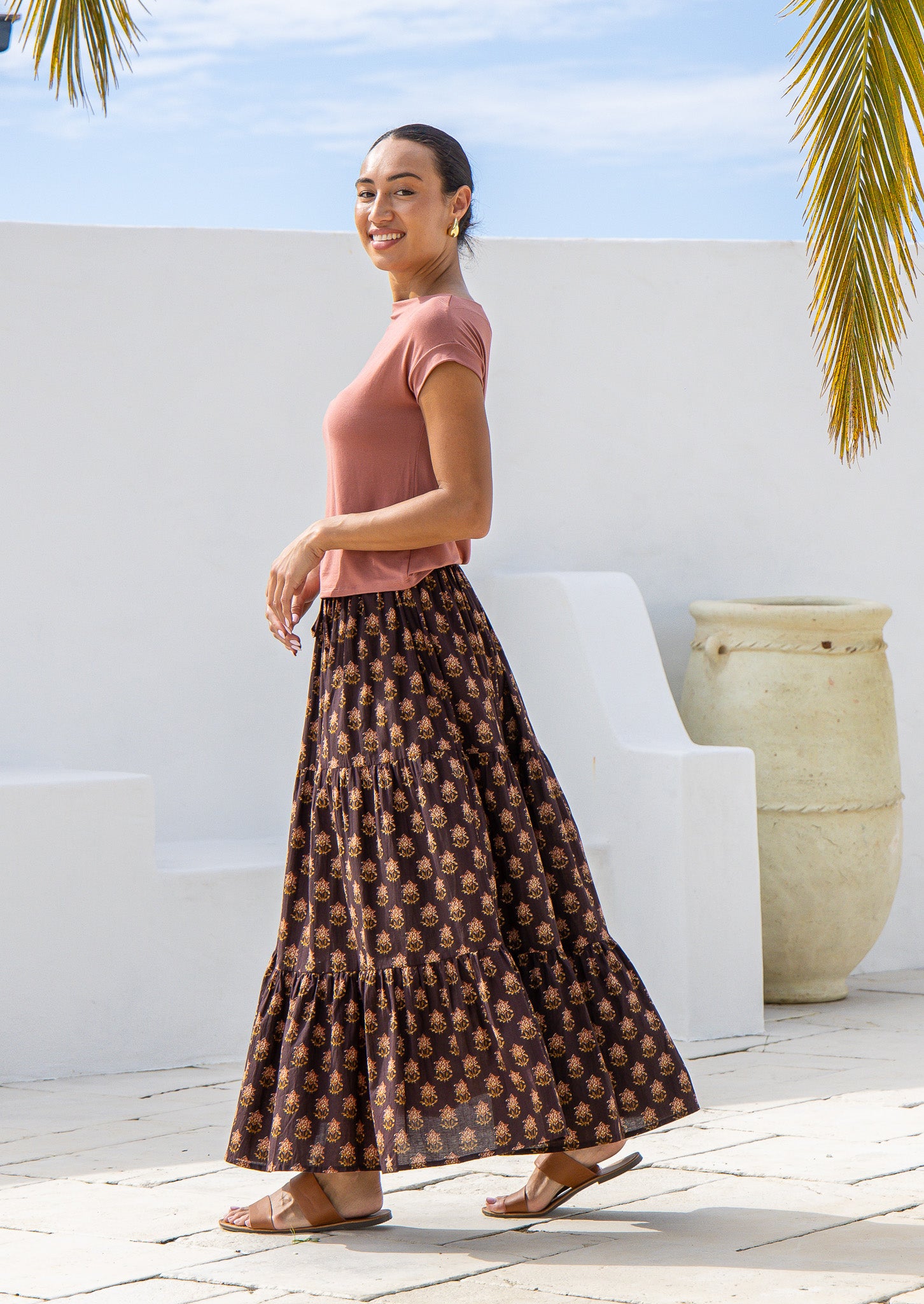 Side pose of model wearing tiered cotton maxi skirt with floral motifs and elasticated waist.
