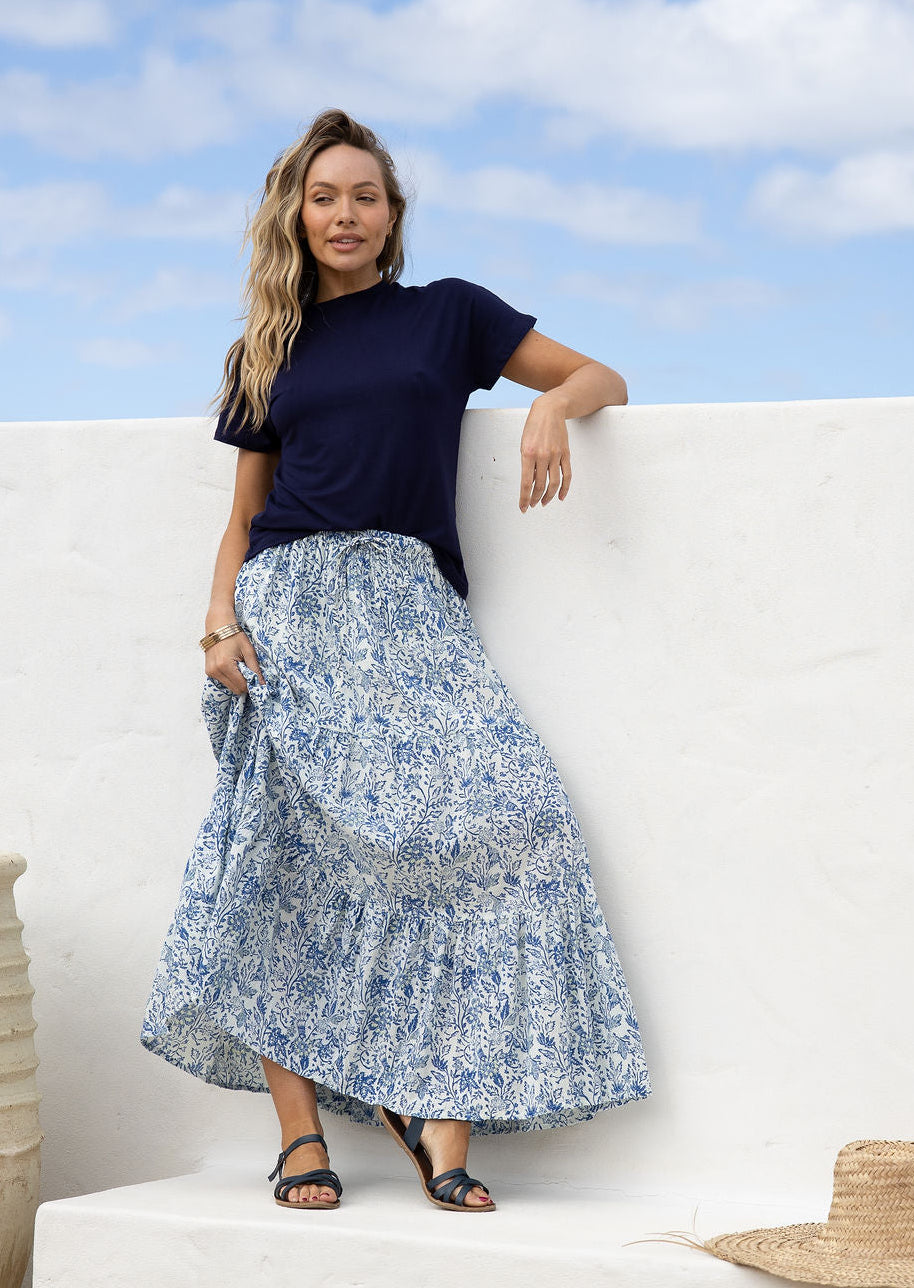 Woman wearing a white based blue floral cotton skirt standing against a white wall.