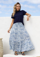 Woman wearing a 100% cotton, white based blue floral cotton skirt standing against a white wall.