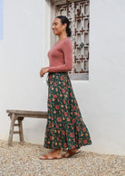 Side pose of model wearing a crinkled cotton skirt with pinky red, cream and orange floral print on dark green base.