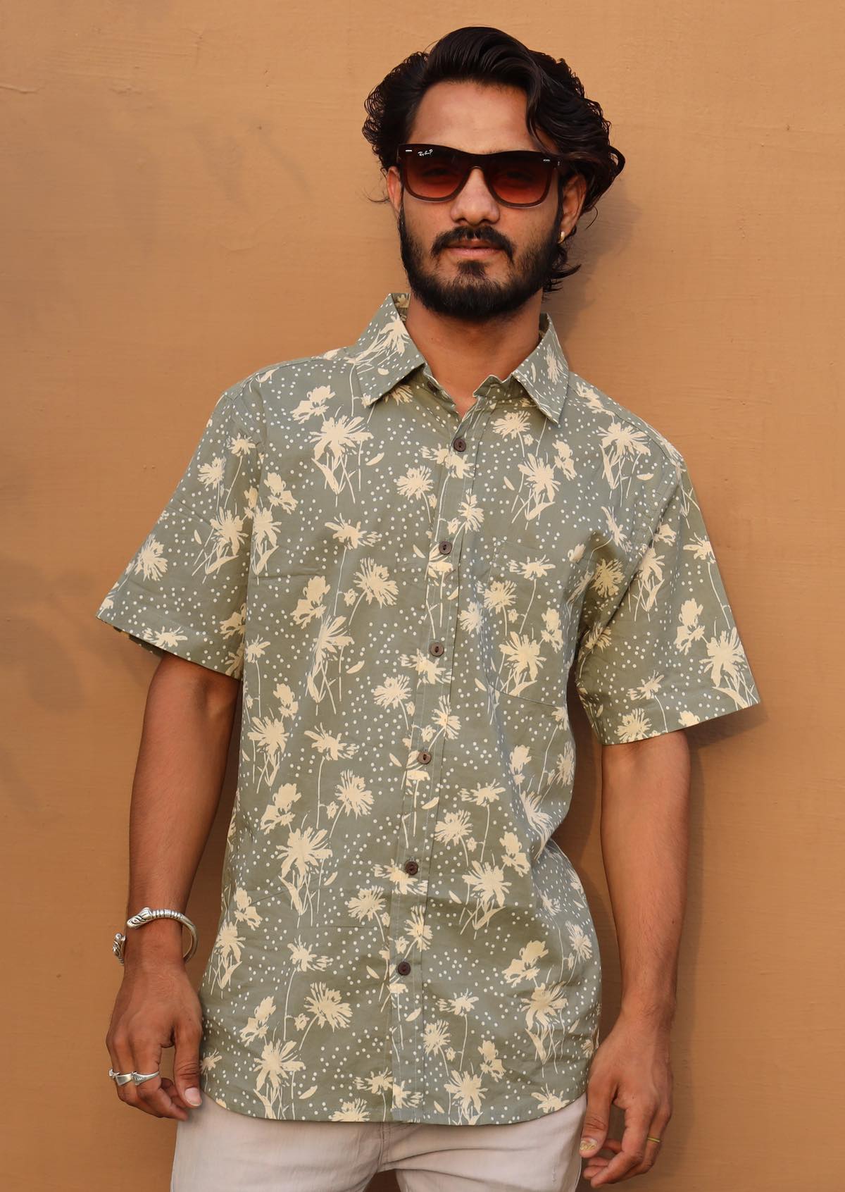 Man poses in short sleeve relaxed fit cotton collared shirt with one breast pocket in pale green based floral print.