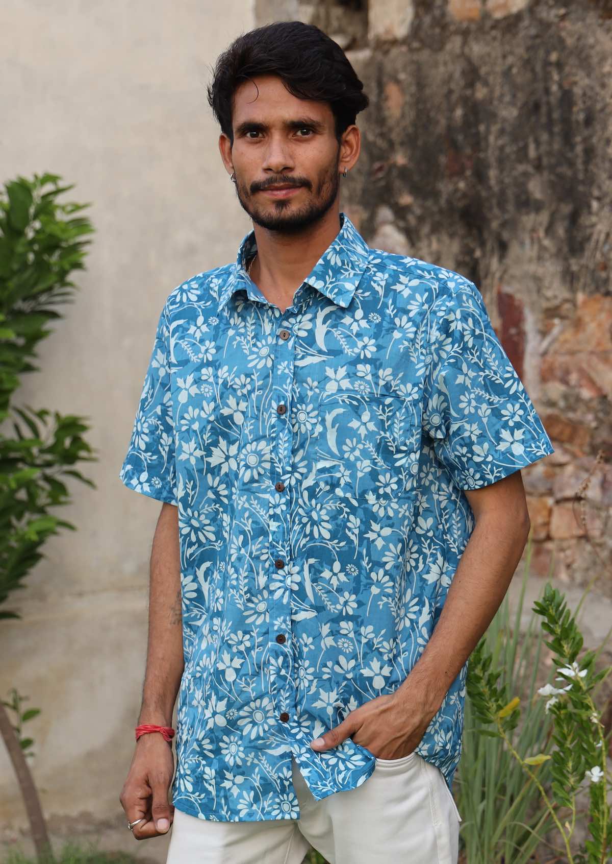 Man wears relaxed fit blue floral print shirt with short sleeves, collar and one chest pocket.