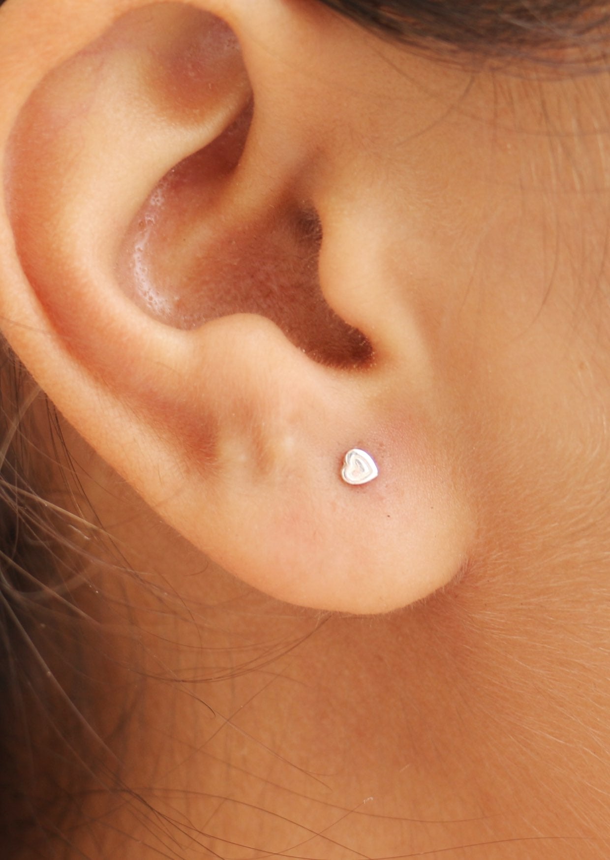A close-up image of a woman wearing delicate small heart studs
