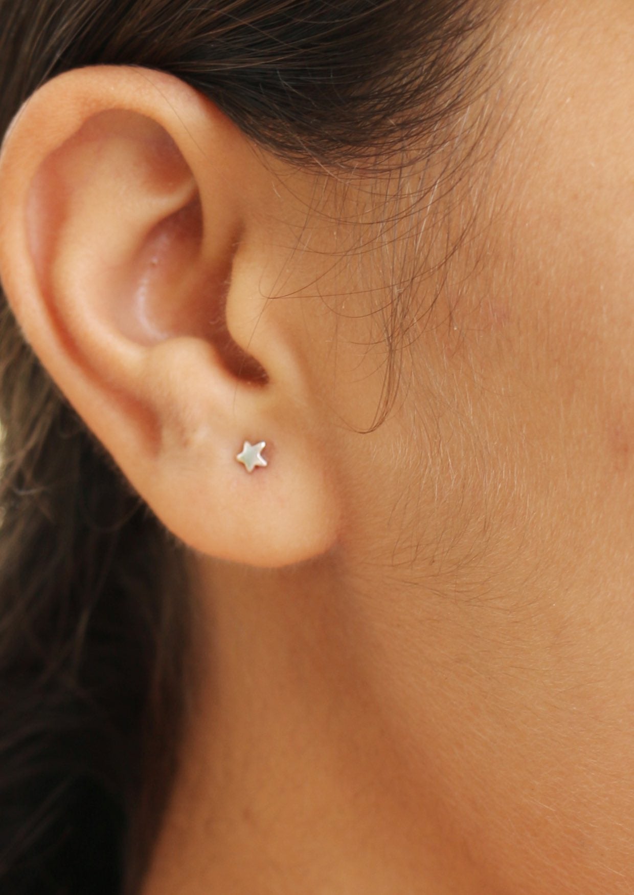 Close up of a woman wearing tiny sterling silver star studs with a minimalist design and secure butterfly backs