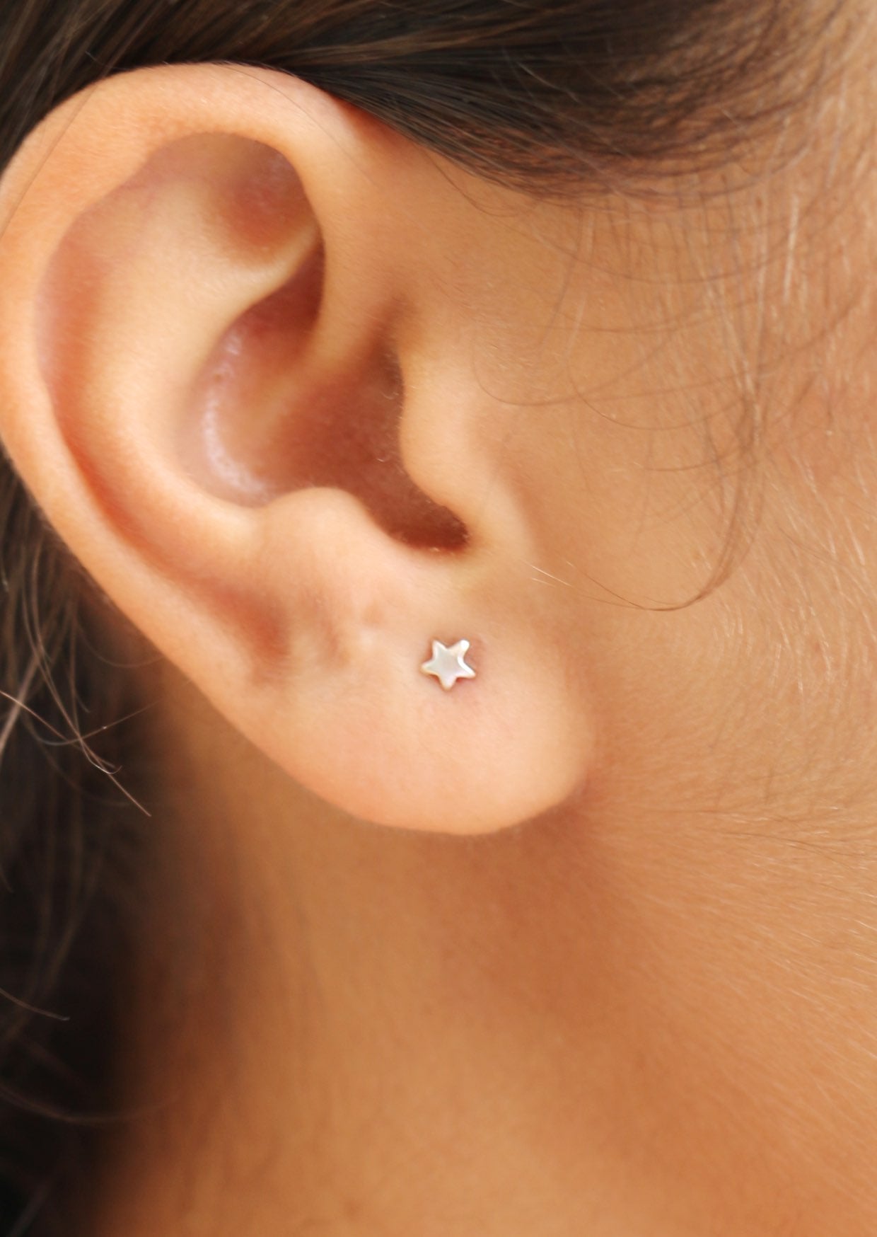 Close-up of an ear wearing a minimalist star shaped silver studs with butterfly backs