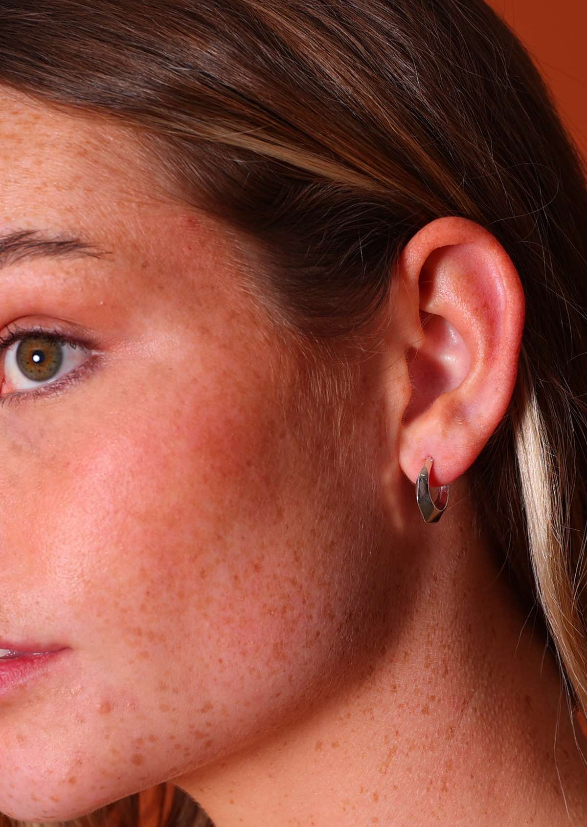 Woman wears sterling silver hollow hoop earrings with six 'sides' and subtle faceting and wire closure