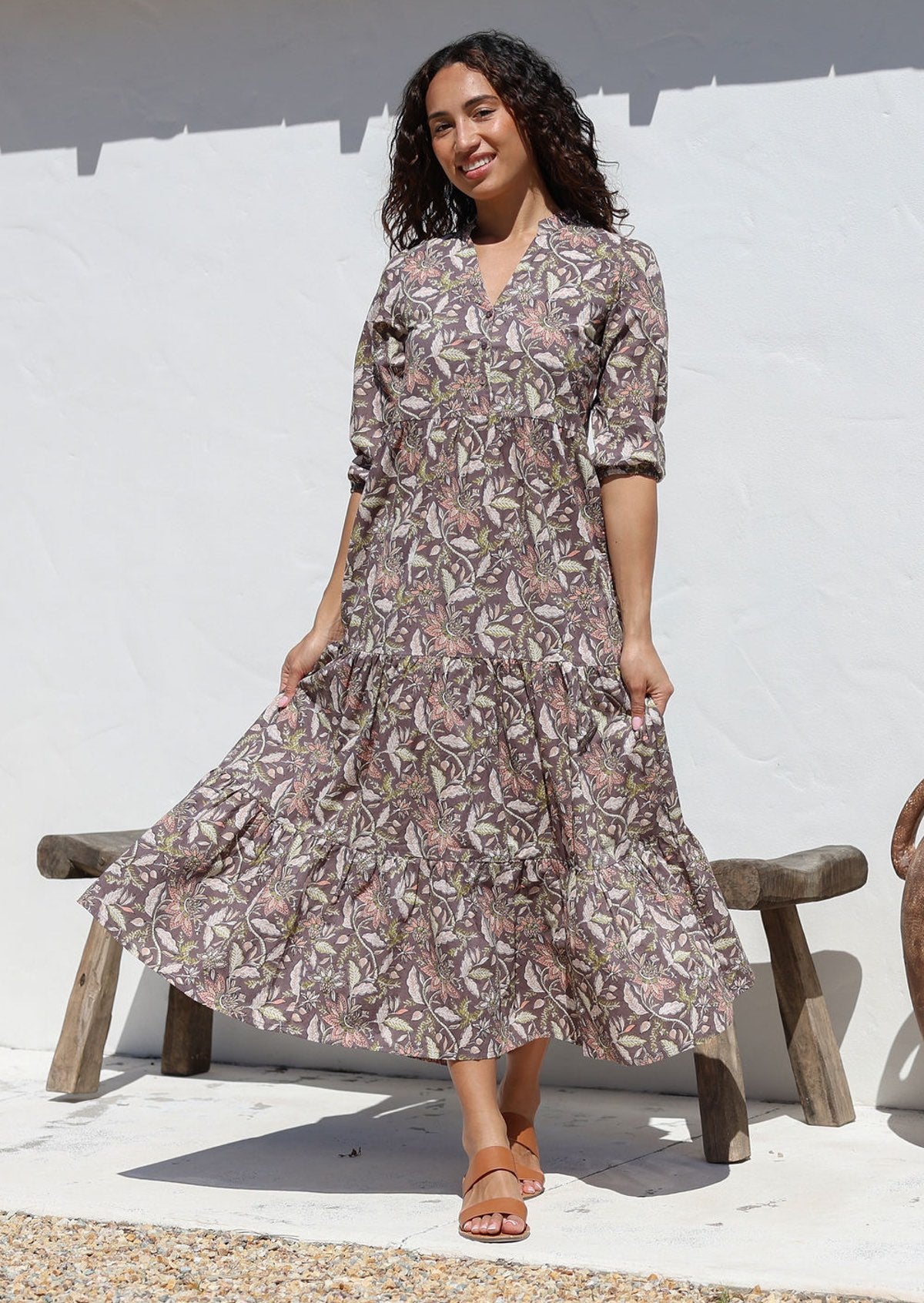 Woman standing against the white wall wears 3/4 sleeved cotton tiered maxi dress with mandarin collar and buttoned bodice