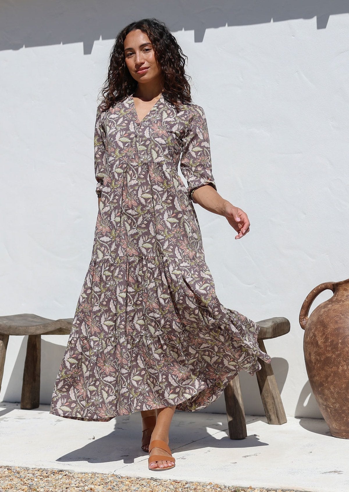 Model poses in taupe based floral maxi dress featuring white, beige, pink and lime green floral print