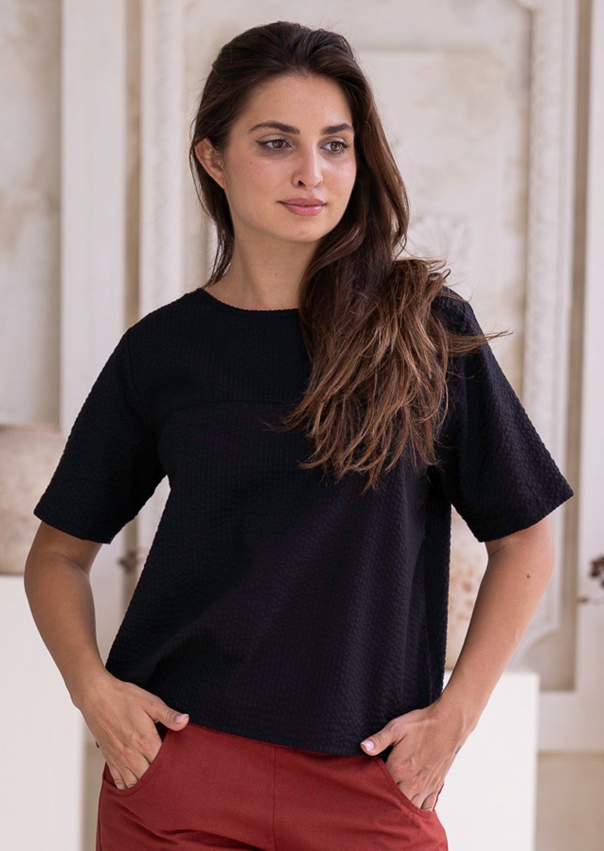 Woman wearing a black non-stretch cotton t-shirt and rust pants standing indoors.